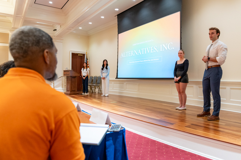Students stand on a stage in front of a screen while members are in the adience.