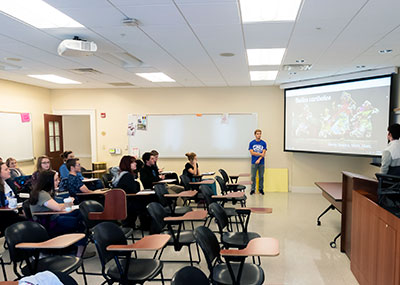 Classroom full of students in Spanish class with two male students standing by a screen giving a presentation on Caribbean dancing
