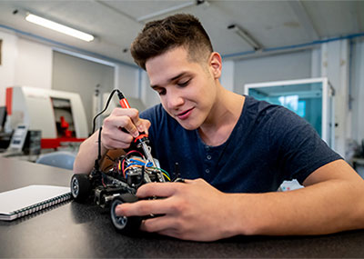 A student uses a soldering gun to work on a robot in a lab classroom