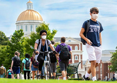 Students facing towards and away from the camera wearing face masks during the change of classes with Christopher Newport Hall in the background