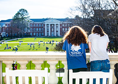 Two girls standing in front of rocking chairs outside CNH looking across the Great lawn towards McMurran