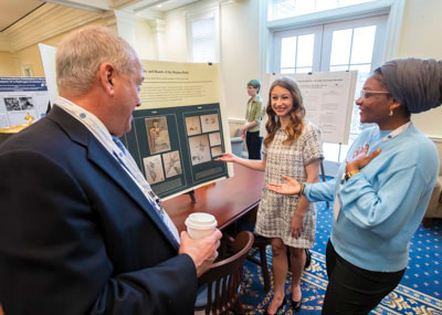 Female student at the Paideia research conference in front of their presentation board discussing research findings with an older male and female