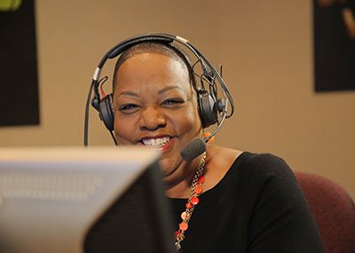 Barbara Hamm Lee wears a headset and smiles while slightly obstructed by a computer monitor