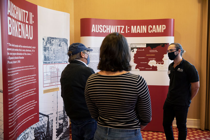 Dr. Richard Freund (left) speaking with Christopher Newport students in front of one of the Auschwitz photo exhibit panels