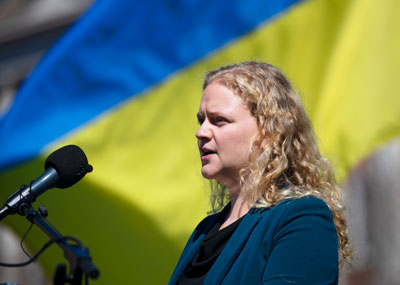 Photo of Dr. Olga Lipatova speaking with the flag of Ukraine behind her