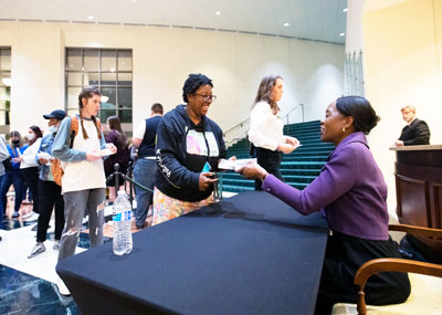 Photo of Margot Lee Shetterly sitting at a table, signing copies of her book for students