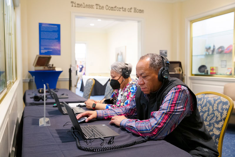 Two local residents sit at computers listening to Hampton Roads Oral History Project material