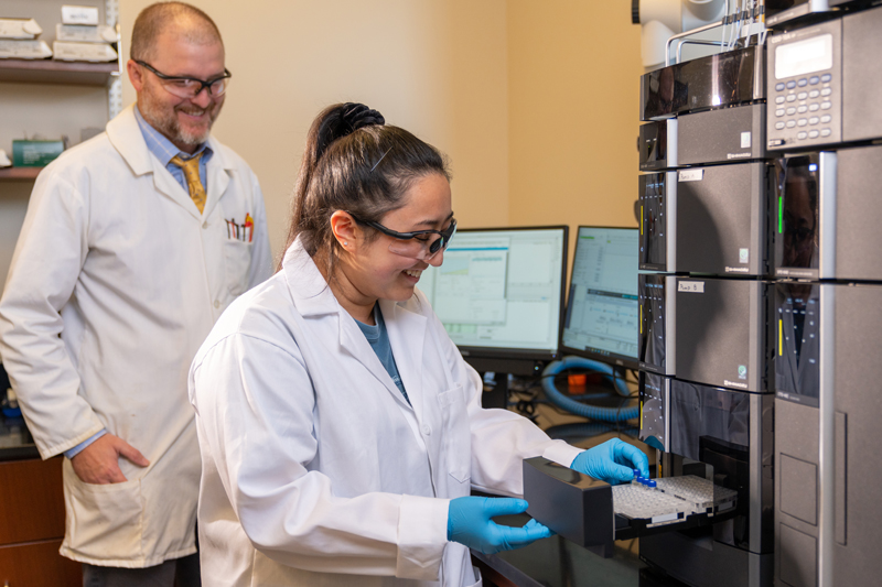 A professor looks on as a student uses a ultra high performance liquid chromatography (UHPLC) instrument