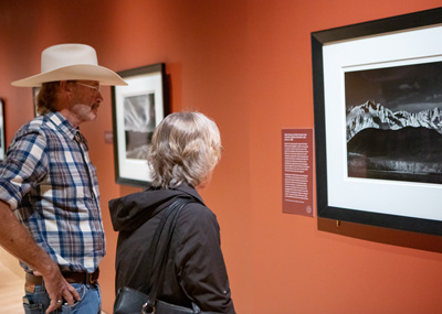 A man wearing a cowboy hat and a woman stare at an Ansel Adams photo in the Torggler Fine Arts Center.
