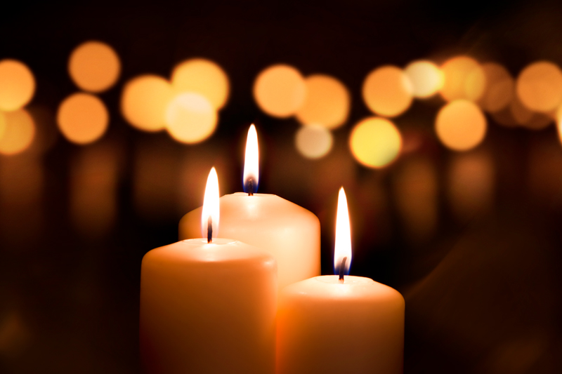 Three lit white candles against a dark background
