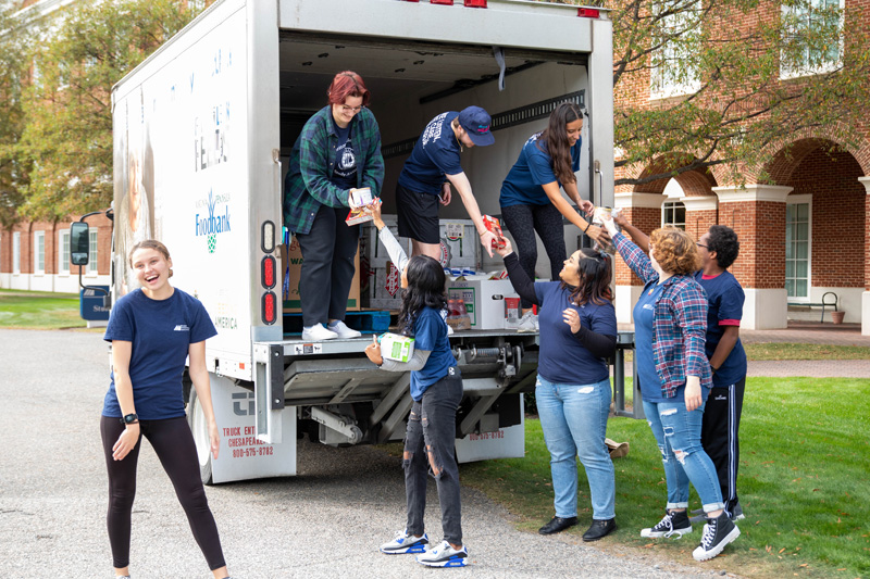 Students hand students standing in the Virginia Peninsula Food Bank truck food to stack.