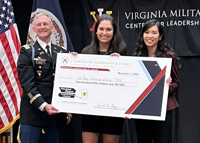 Two students stand beside a man in military uniform holding a large check with their names on it.