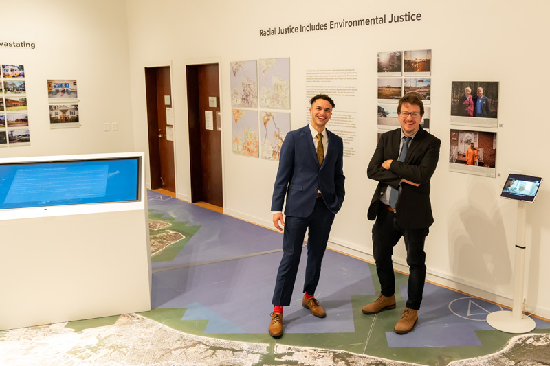 Brandon Davis '22 and Dr. Johnny Finn stand amongst the multi-media exhibition 'Living Apart: Geography of Segregation in the 21st Century'