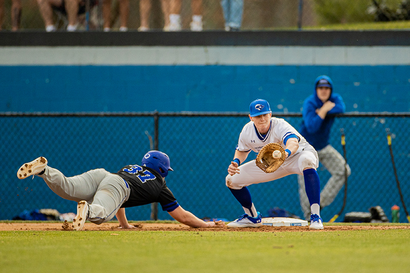 A CNU baseball player holds open his glove to catch a ball while an opponent tries to tag the base. 
