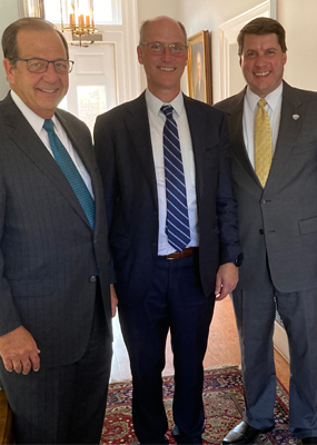 Three men in suits stand and smile for a photo.