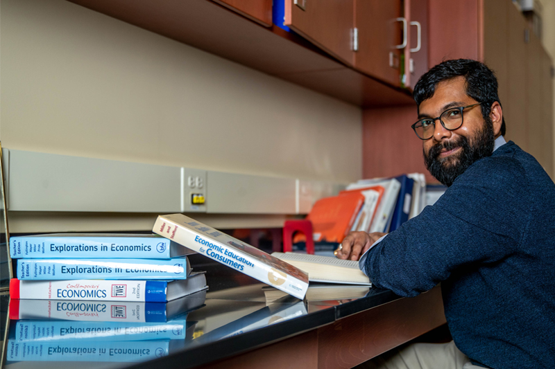 Dr. Rik Chakraborti sits amongst books on economics while looking at a camera.