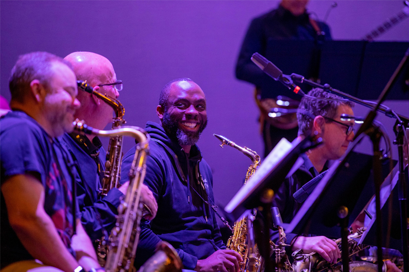 Nii Akwei Adoteye smiles while holding his saxophone amongst band members.