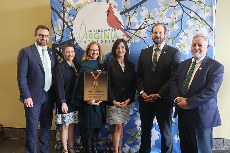 Individuals are gathered around one person holding a certificate of the award.