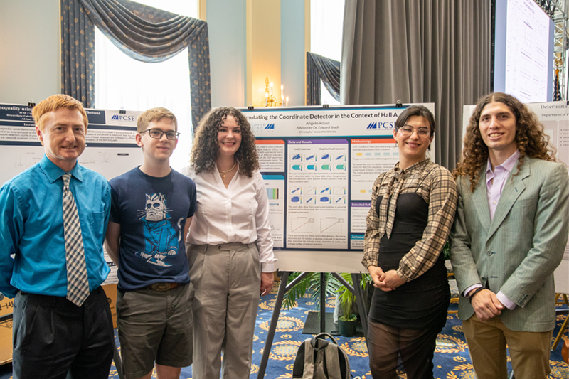 Associate Professor Monaghan stands with four students in front of a backboard on display.