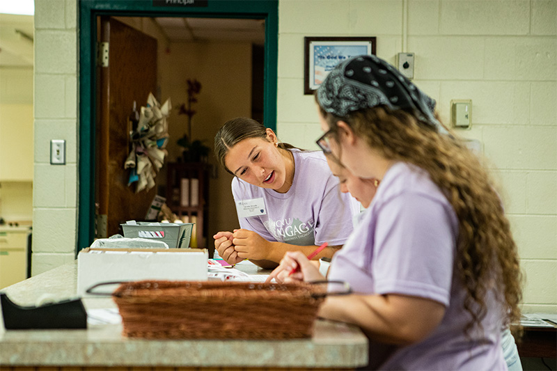 A student leans on a countertop while looking at something with other students who are out of focus.