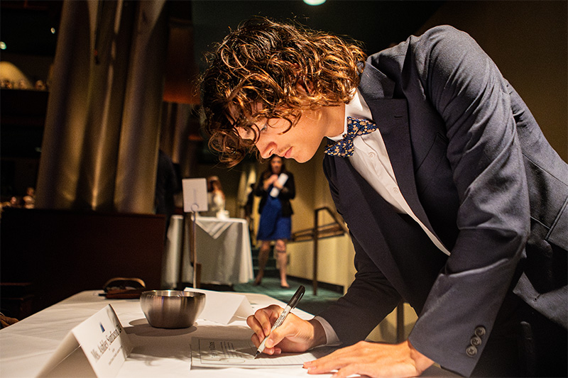 Ryan Terrell '27 signs the Christopher Newport Honor Code wearing a suite and bow tie for the occasion. 