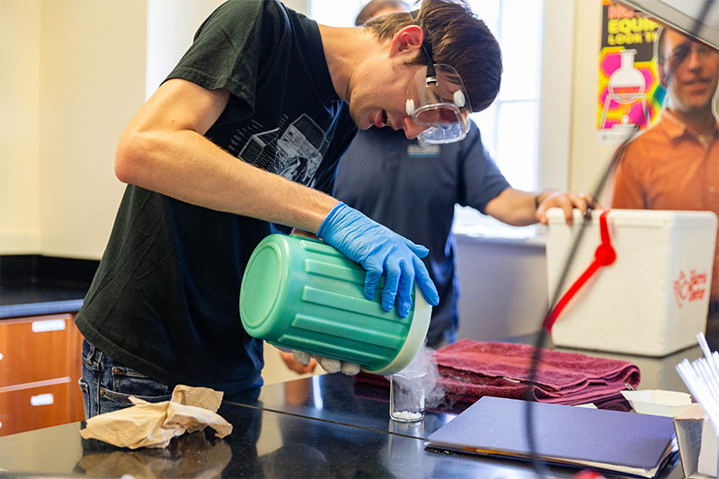 A student pours liquid nitrogen into a container in a lab.