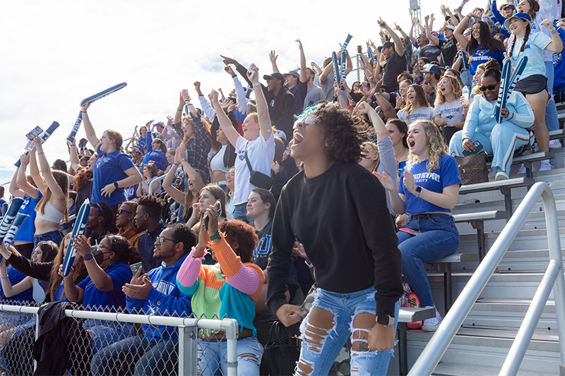 Christopher Newport students stand and cheer during a football game.