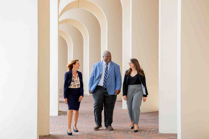 Three individuals in business attire walk through a colonnade. 