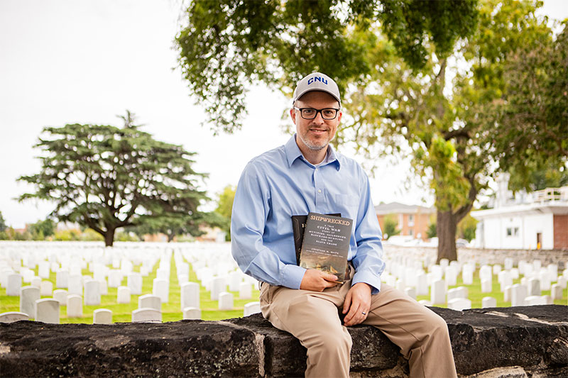 Jon White sits on a wall with a cemetery in the background.