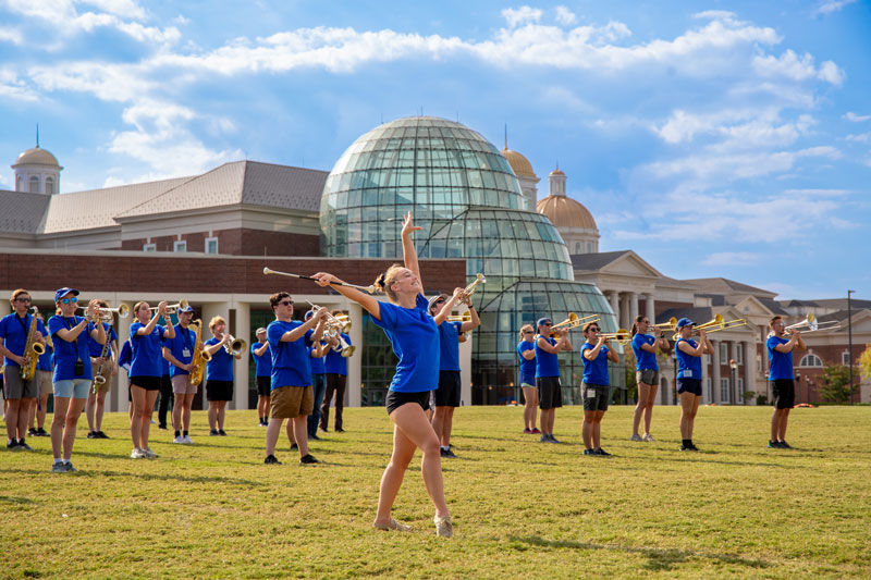 The Marching Captains practice on a field with the cupolas of the Torggler Fine Arts Center, Trible Library and Christopher Newport Hall in the background.