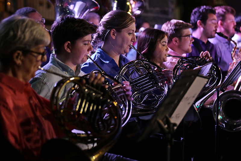 The horn section of the Christopher Newport University wind ensemble are lit at night while performing.