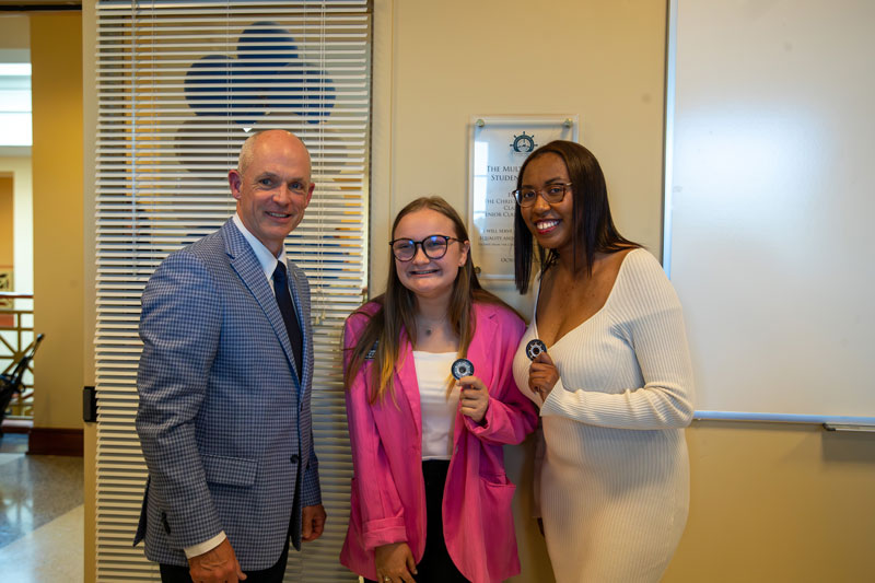 CNU President William G. Kelly stands beside Louise Byrne '23 and Kayla Caine '23 in front of a plaque that adorns the wall of the new multicultural center.
