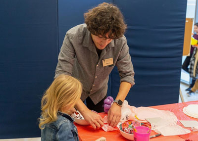 A young child is helped by a student during one of the Torggler Fine Arts Center's Family Fun Day.