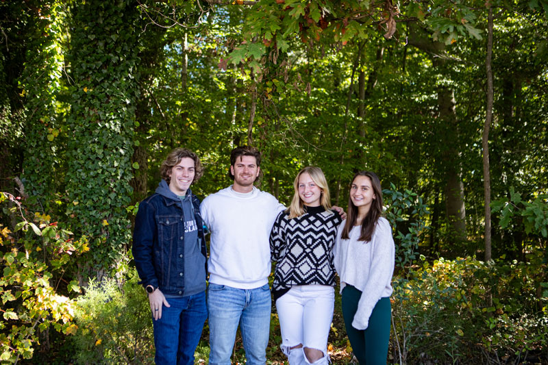 Four students stand in front of a lush forest background.
