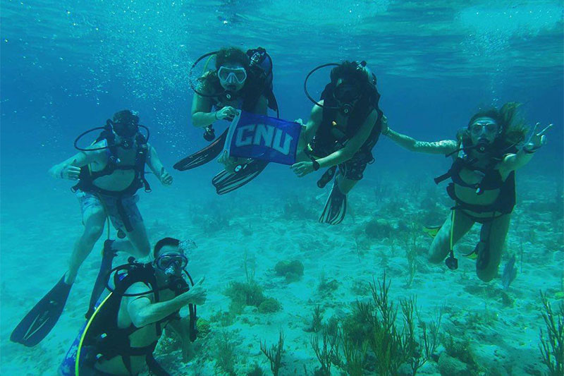 Students in snorkel gear hold a CNU flag underwater.