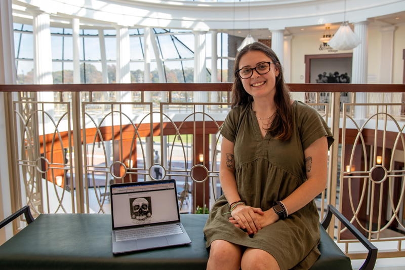 Brooke Patten sits to the left of a laptop that displays her research.