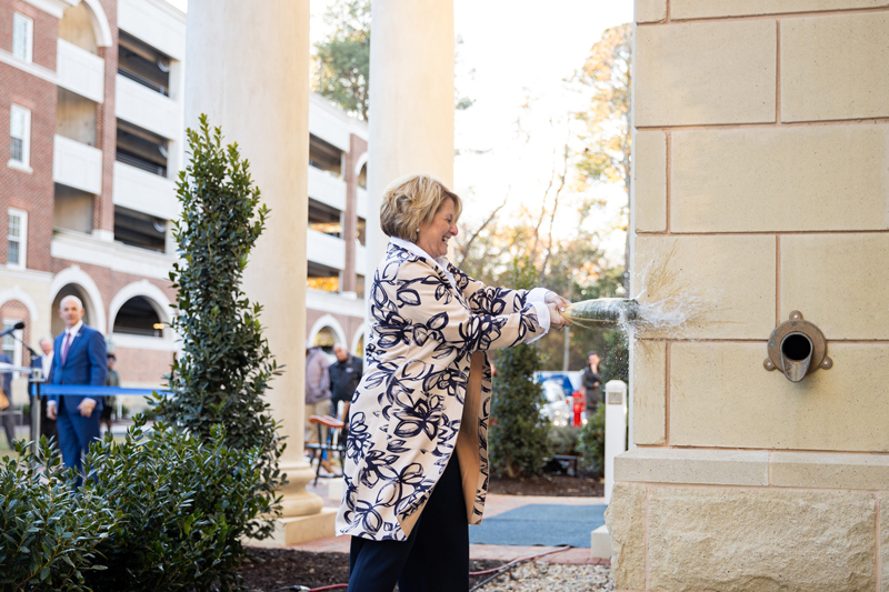 First Lady Angie Kelly smashes a bottle of champagne against the new administrative offices building. Her husband, university President Bill Kelly watches in the background.