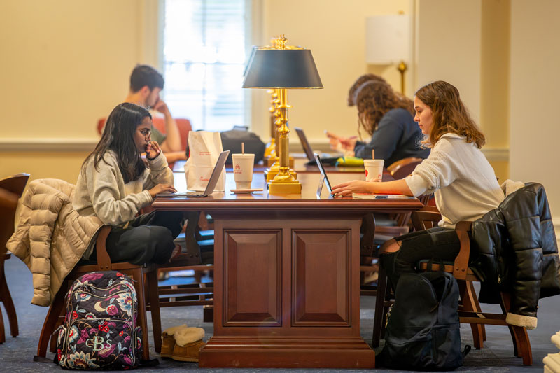 Two students sit at a table across from one another studying.