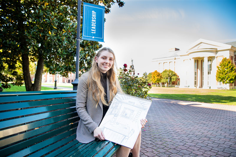 Madeline Renaux sits on a bench while holding a sketch that's used in a professor's book.
