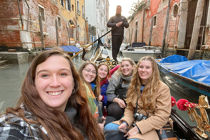 Abbigail Traylor, left, takes a selfie with other students and professors while riding in a gondola in Italy being steered by a man in all black