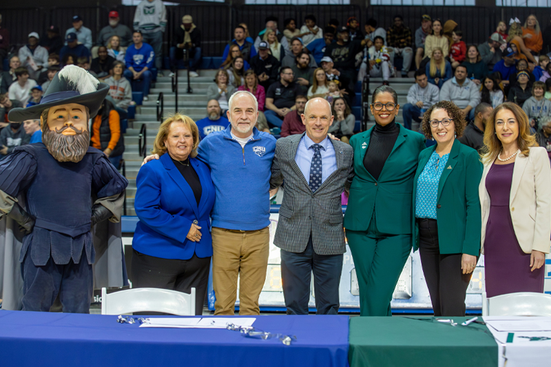 Captain Chris stands to the left of a group of CNU and VPCC representatives after signing an agreement on a basketball court.