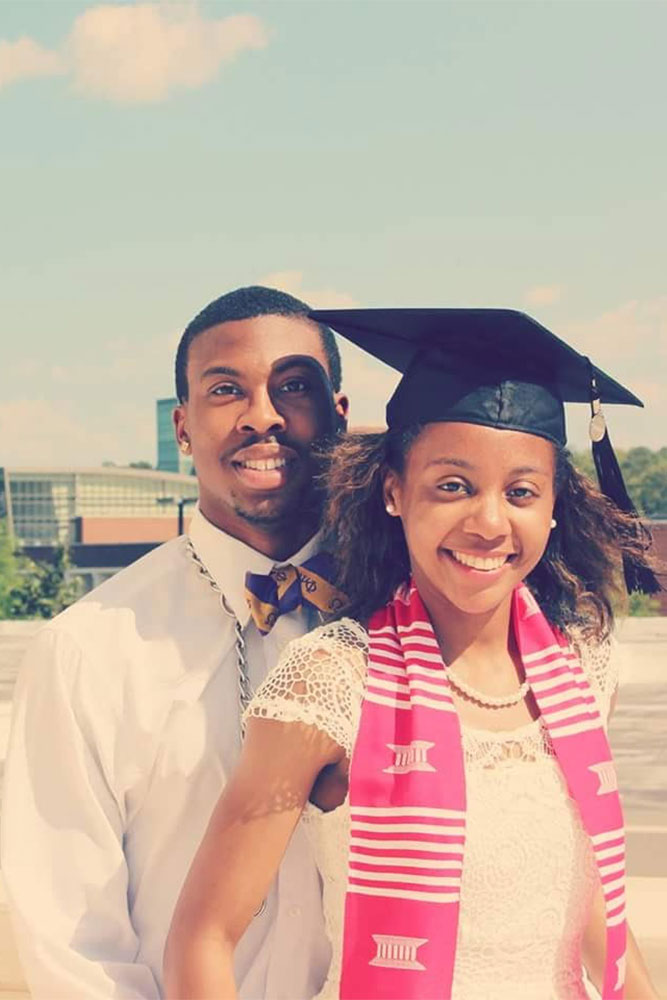 Shomari and Leah standing on the top of a building. Leah is wearing a stole and her graduation cap.