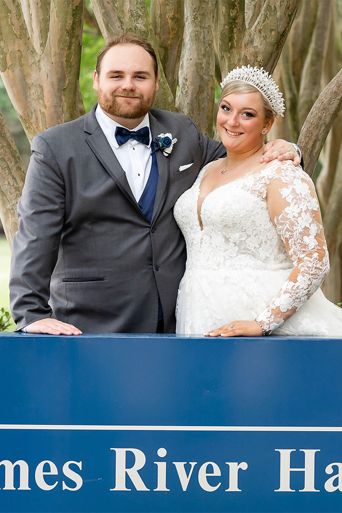 Nick and Malory stand in front of the James River Hall sign as groom and bride