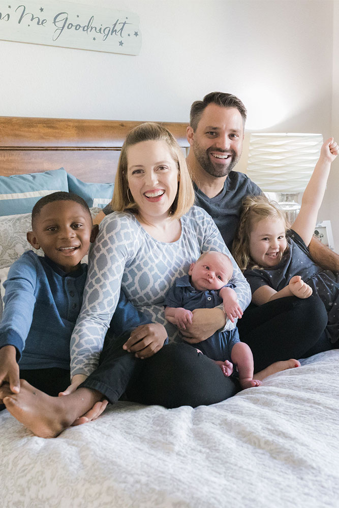 Melody and Zach sit on their bed with their three children