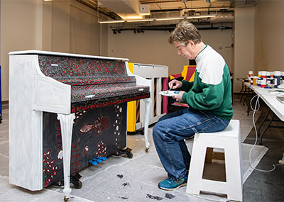 Scott Turner sits at his piano as he paints it.