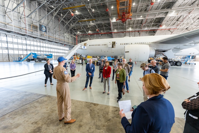 A group of people standing in front of an airplane and listening to a NASA official 