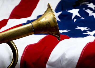 A brass bugle in the foreground and an American flag in the background.