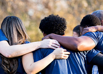 Group of diverse individuals with arms around each other wearing blue shirts