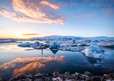 Icelanding landscape with glaciers strewn about on a beach and bright orange rays from the sun.