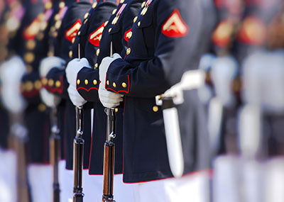 White gloved hands of Marine Corps members in their dress blues hold their rifles at rest.